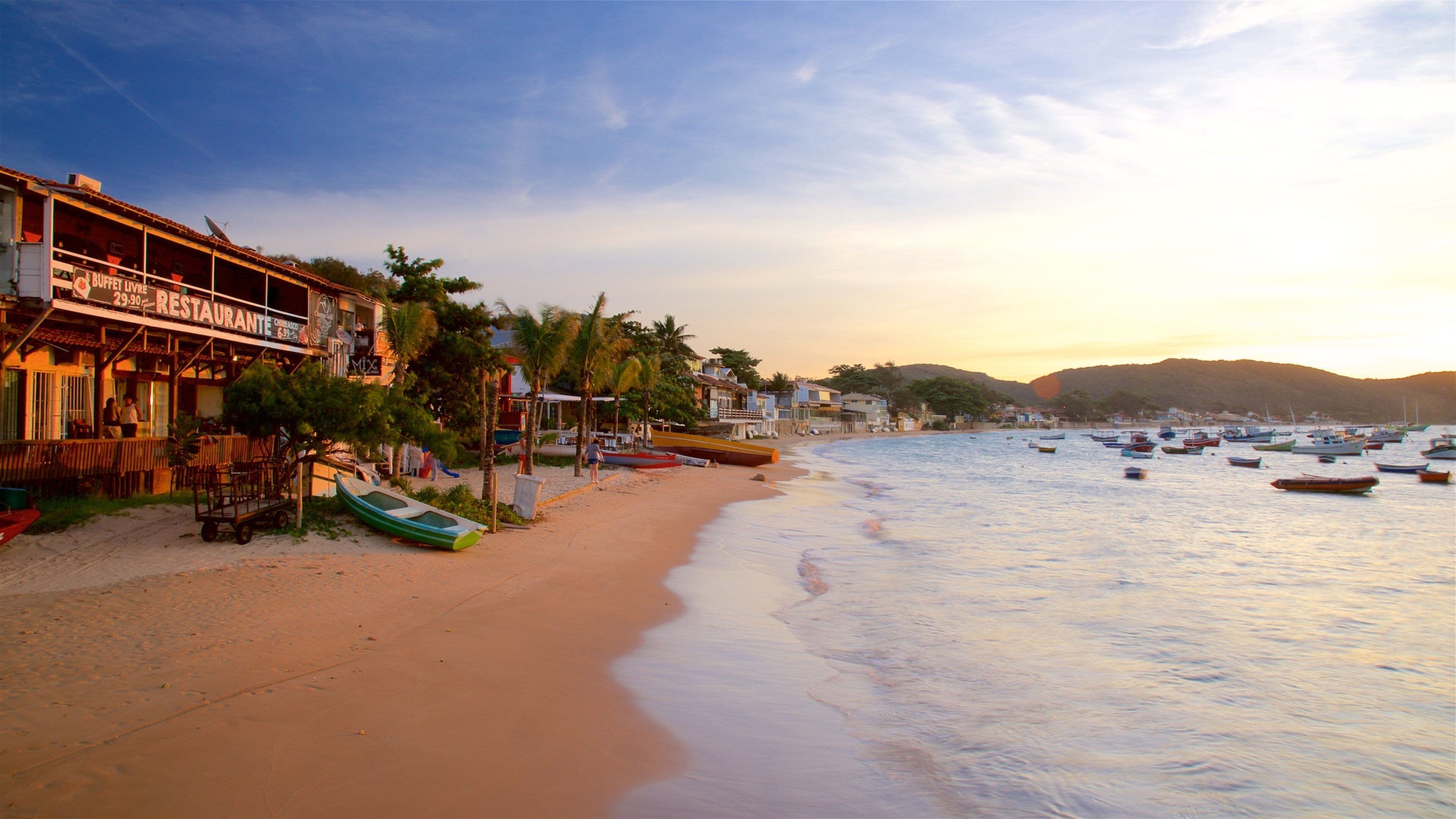 Praia em frente à pousada com oceano e barcos ao entardecer